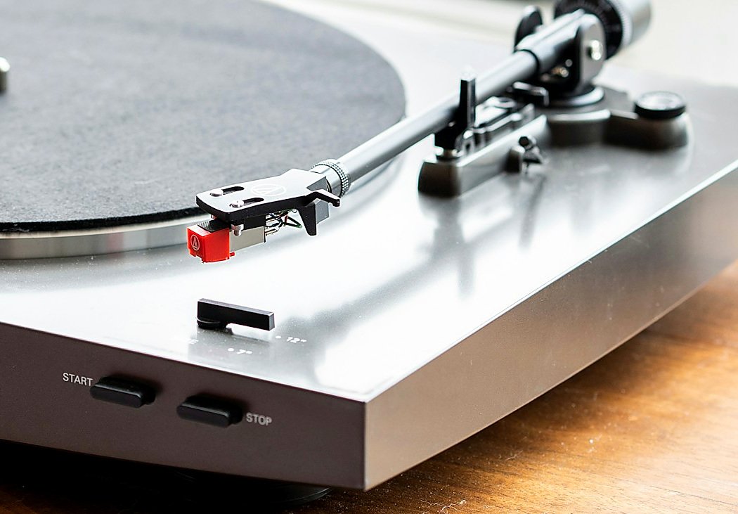 A turntable tonearm resting over the platter, on a wooden table in soft window light.