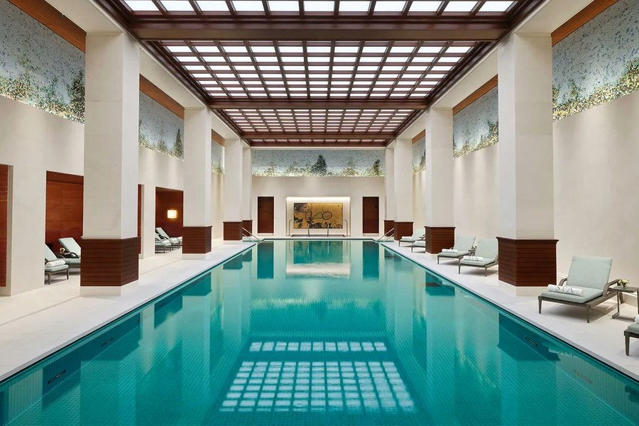 The indoor pool of a spa, daylight through a coffered glass roof, loungers along both sides.